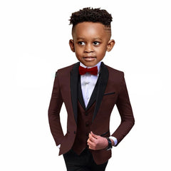 A young boy wears a formal three-piece suit featuring a brown blazer with black shawl lapels.