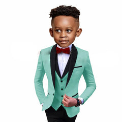 A young boy wears a mint green three-piece suit with a black shawl lapel and a red bow tie.