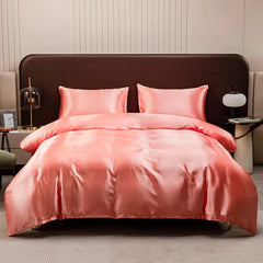 A solid coral pink satin duvet cover set with two matching pillowcases on a bed.