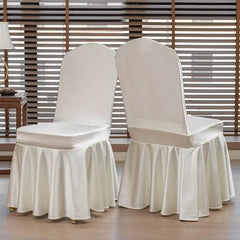 Two white satin chair covers with pleated skirts displayed in a room with window blinds.