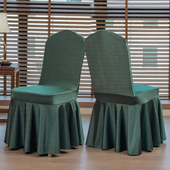 Two dark green satin chair covers with pleated skirts displayed in a room with window blinds.