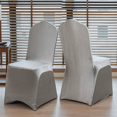 Two silver satin chair covers with a pointed top design displayed on chairs in a room.