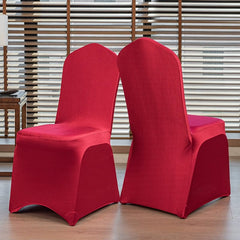 Two red satin chair covers with a rounded top design displayed on chairs in a room.
