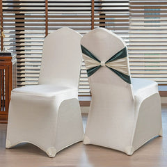 Two white chair covers with a decorative dark green and cream satin bow on the back.
