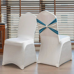 Two white chair covers with a blue satin bow tie displayed in front of window blinds.