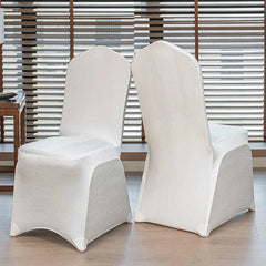 Two white satin chair covers with a pointed top design displayed in a bright room.