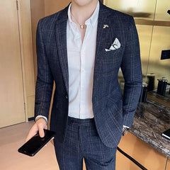 A man wears a slim-fit navy blue plaid suit jacket and matching trousers with a white shirt.
