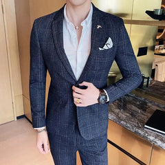 A man wears a dark grey plaid two-piece suit with a white button-down shirt and a pocket square.