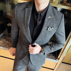A man wears a grey plaid two-piece suit with a black button-down shirt and a pocket square.