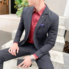 A man wears a slim-fit dark grey suit with a red button-down shirt and a pocket square.
