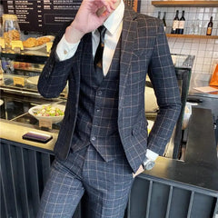 A man wears a dark grey plaid three-piece suit with a white shirt and black tie.