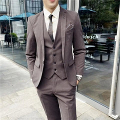 A man wears a slim-fit brown three-piece suit with a white shirt and a dark tie.