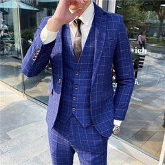 A man wears a blue three-piece suit with a white shirt and a dark tie in a windowed setting.