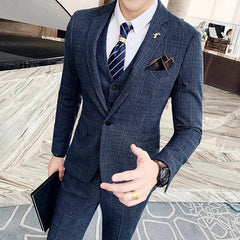 A man wears a navy blue plaid three-piece suit with a white shirt and a striped tie.