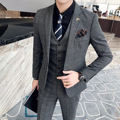 A man wears a grey plaid three-piece suit with a black shirt and a striped tie.