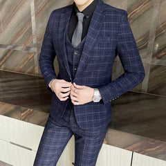 A man wears a navy blue plaid three-piece suit with a black shirt and grey tie.