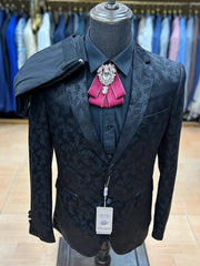 A black floral jacquard three-piece suit with a maroon brooch on a black dress shirt.