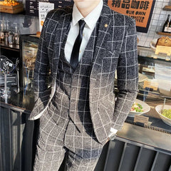 A man wears a charcoal grey plaid three-piece suit with a white shirt and black tie.