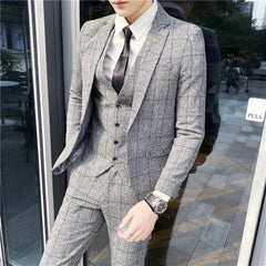 A man wears a grey plaid three-piece suit with a white shirt and a dark tie.