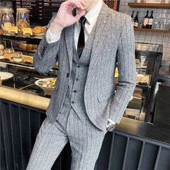A man wears a grey striped three-piece suit with a white shirt and black tie.