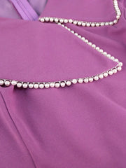 A close-up of a purple dress featuring a V-neckline adorned with a delicate string of pearls.