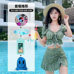 A woman wears a green plaid two-piece swimsuit with a skirt, accompanied by a set of swimming accessories.