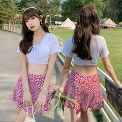 A two-piece swimsuit featuring a white cropped top and a red heart-patterned skirt.