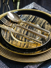 A black and gold patterned dinner plate is set with gold-toned cutlery on a textured gold charger.
