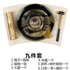 A luxury black and gold dinnerware set featuring a plate, placemat, chopsticks, napkin, and tea cup.