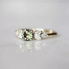 A delicate gold-tone ring featuring a round olive green zircon flanked by leaf-shaped crystals.