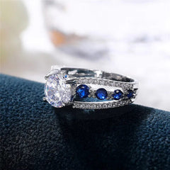 A silver-tone ring featuring a large round white cubic zirconia flanked by blue accent stones.