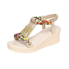 A gold platform wedge sandal featuring a floral braided strap adorned with rhinestones.