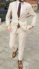 A man wears a beige two-piece suit with a patterned tie and brown loafers.