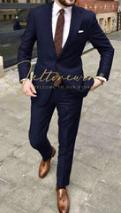 A man wears a navy blue two-piece suit with a patterned tie and brown leather loafers.