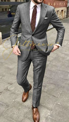 A man wearing a grey two-piece suit with a white shirt, patterned tie, and brown loafers.