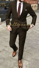 A man wearing a dark brown two-piece suit with a white shirt, patterned tie, and brown loafers.