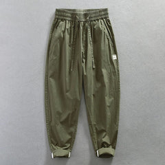 Olive green loose-fit cotton trousers with an elastic waistband and a small side badge.