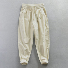 Beige loose-fit cotton trousers with an elastic waistband and a small badge detail.