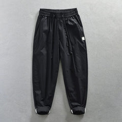 Black loose-fit cotton trousers with an elastic waistband, drawstring, and cuffed hems.
