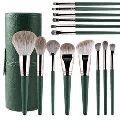 A set of fourteen green makeup brushes with soft bristles and a matching cylindrical storage case.