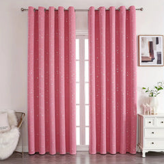 Pink blackout curtains with silver star patterns and grommet tops hanging on a window.