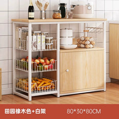 A light wood-toned kitchen storage rack with a white metal frame, featuring three wire baskets, a cabinet, and a top shelf.
