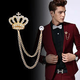 A gold-tone crown brooch with rhinestone accents and a double chain worn on a maroon suit.
