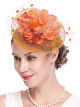 A woman wears an orange fascinator hat featuring a large fabric flower and a decorative mesh veil.