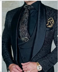 A man wears a black three-piece suit with a patterned jacket, shawl lapel, and paisley tie.