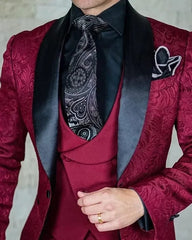A man wears a burgundy patterned three-piece suit with a black shawl lapel and paisley tie.
