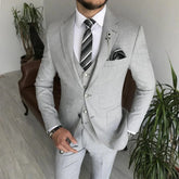 A man wears a light gray three-piece suit with a white shirt and a striped tie.