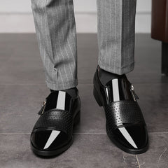 A pair of black pointed-toe dress shoes with a perforated leather panel and side zipper closure.