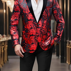 A man wears a red and black paisley patterned blazer with a black lapel and one button closure.