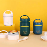 Three portable stainless steel thermal lunch boxes in white, green, and blue sit on a table.